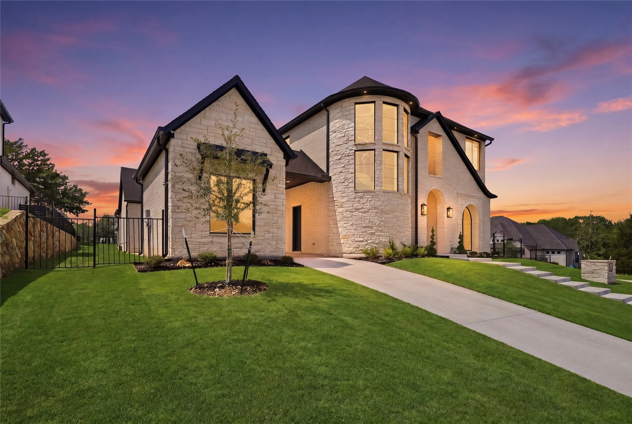 Stone facade residence featuring a prominent turret with large windows, arched entryway, and a sloped concrete driveway