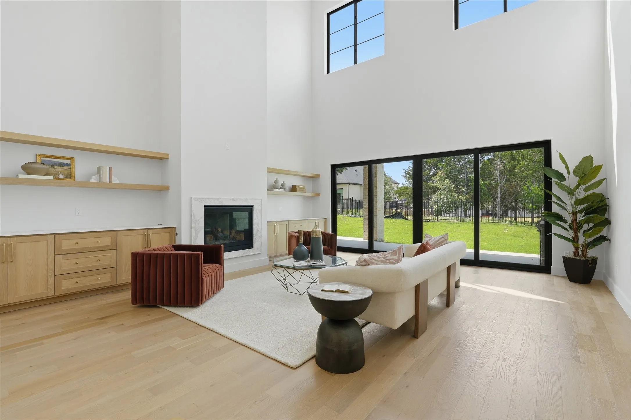 Spacious living area featuring high ceilings, light wood-finish flooring, and a fireplace with a light-toned surround