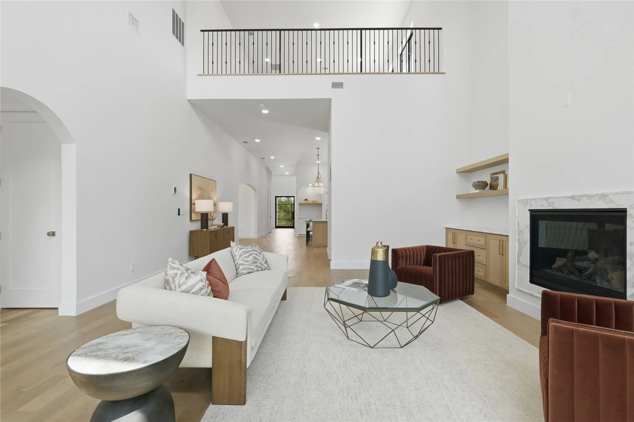 Open-concept living space featuring soaring vaulted ceilings, light wood-finish flooring, and a second-story interior balcony with black metal railings
