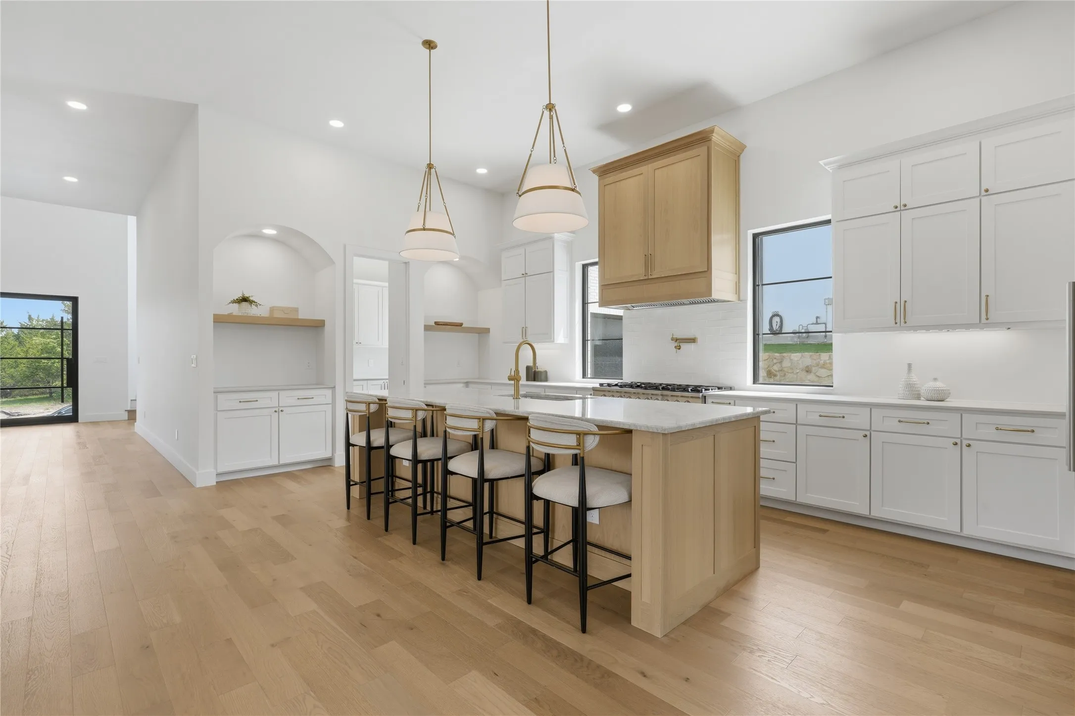 Kitchen featuring an expansive island with seating, pendant lighting, wood-finish flooring, white cabinetry, and stainless steel appliances