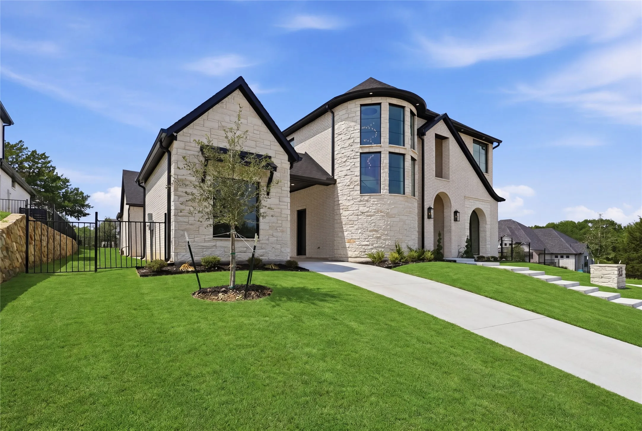 Contemporary stone exterior featuring a circular turret with tall windows, a prominent arched entry, a concrete driveway, and manicured landscaping