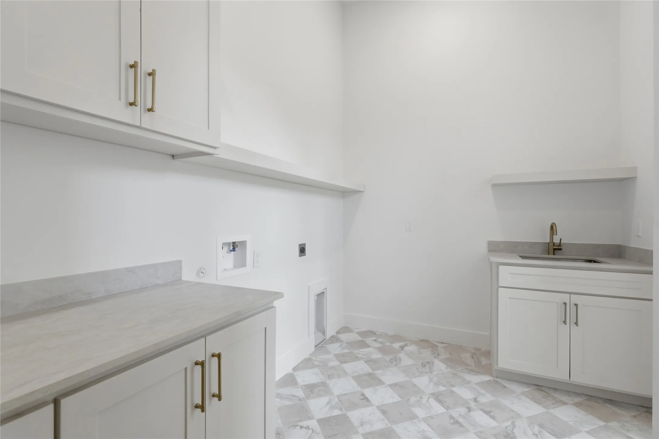 Utility room featuring checkerboard tile flooring, white cabinetry with gold-toned hardware, light-toned countertops, and a utility sink with a brass-finish faucet