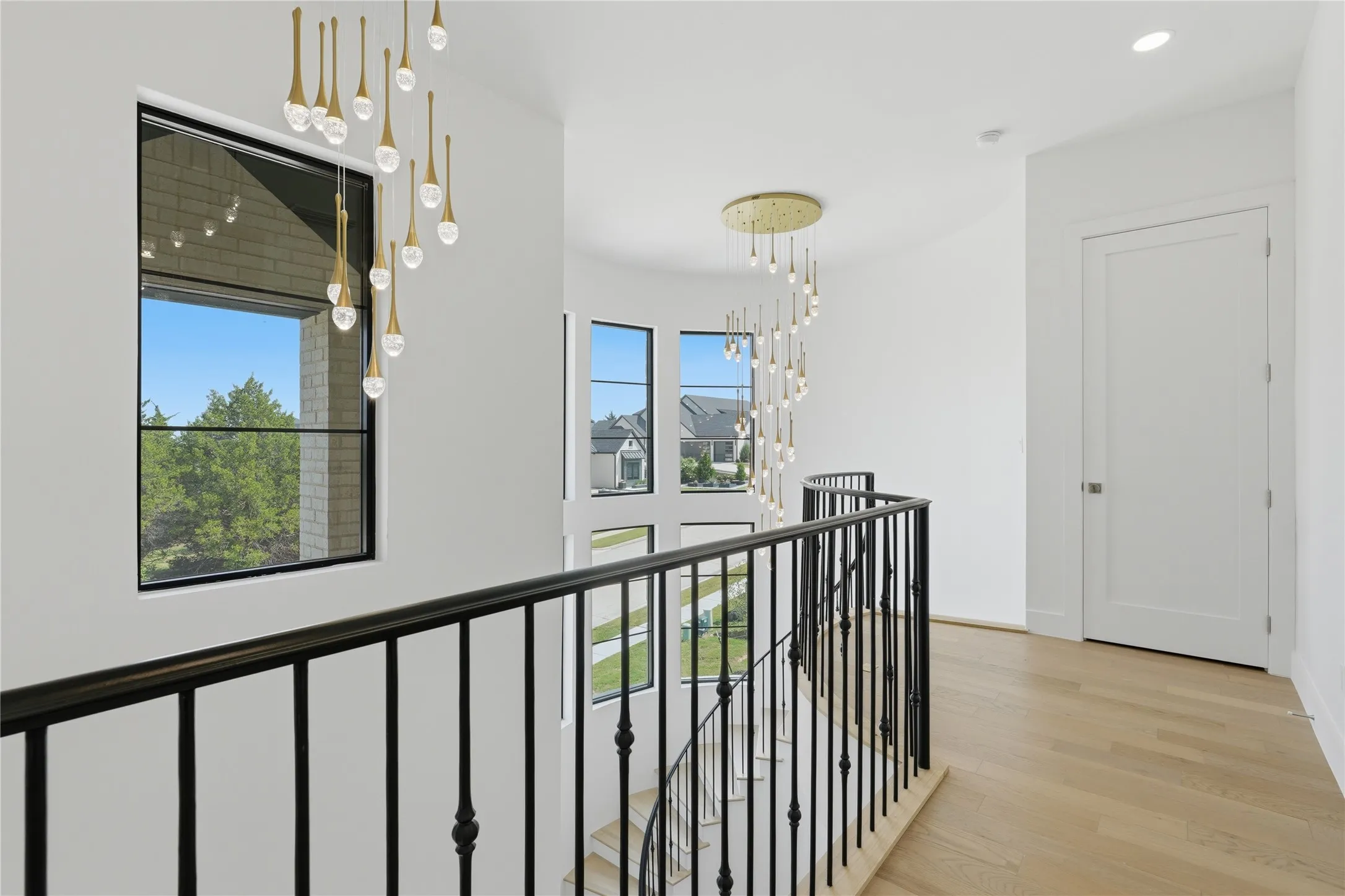 Upper-level landing featuring light wood-finish flooring, white walls, and a black wrought-iron railing