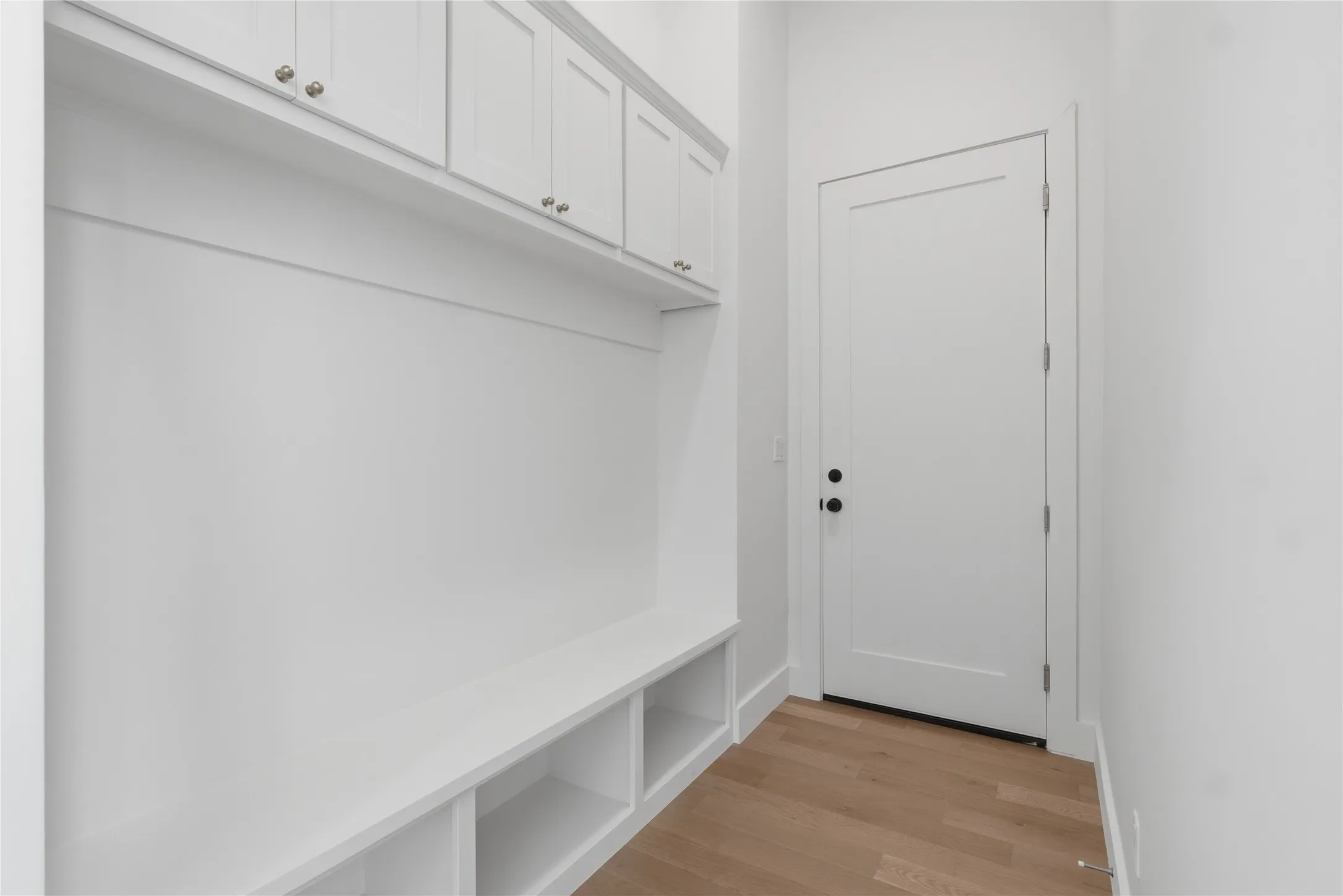 Built-in mudroom bench with cubby storage, upper cabinetry with brushed nickel hardware, and wood-finish flooring