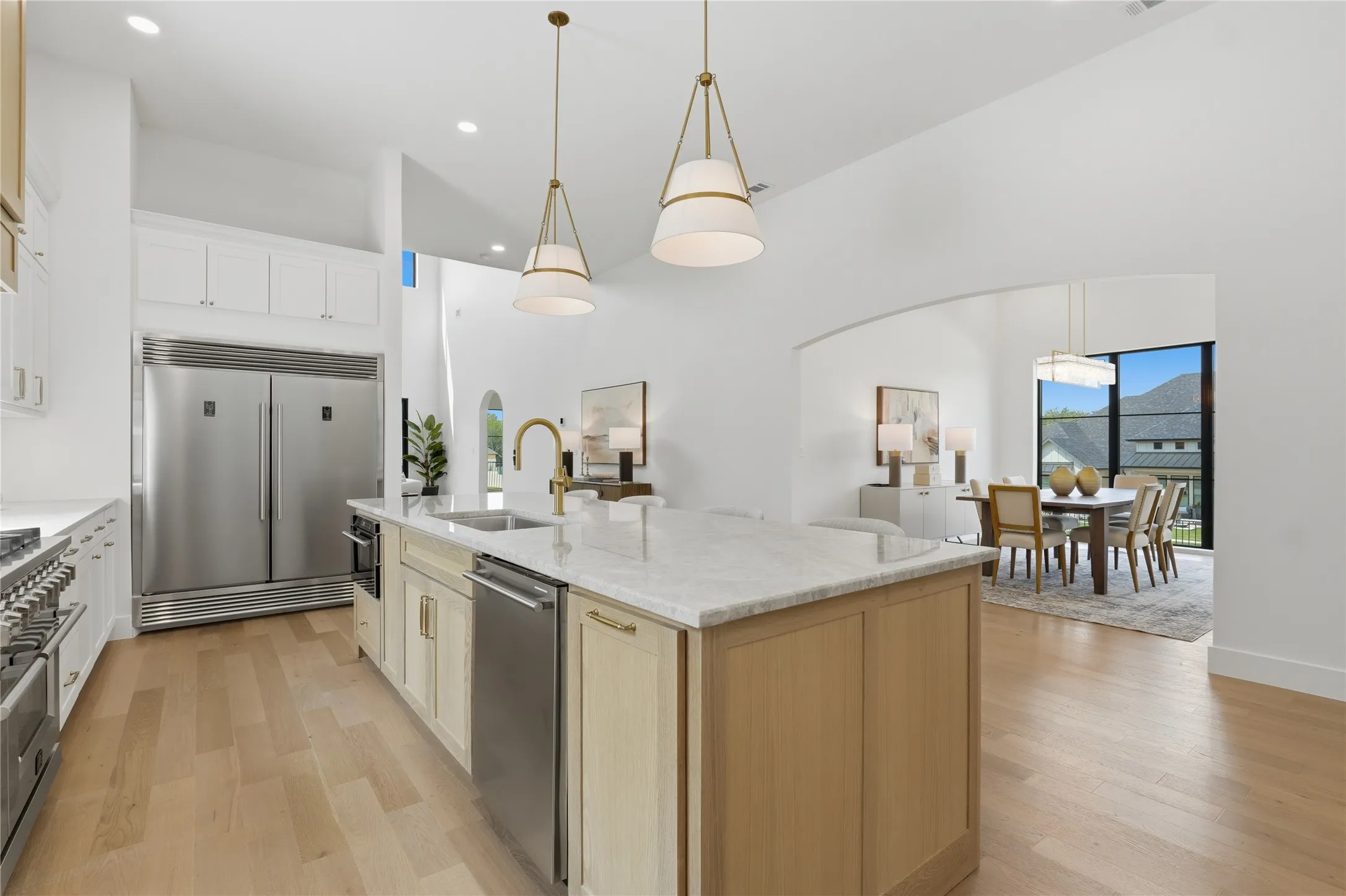 Gourmet kitchen featuring a large central island with integrated sink, stainless steel appliances, light wood-finish flooring, and pendant lighting