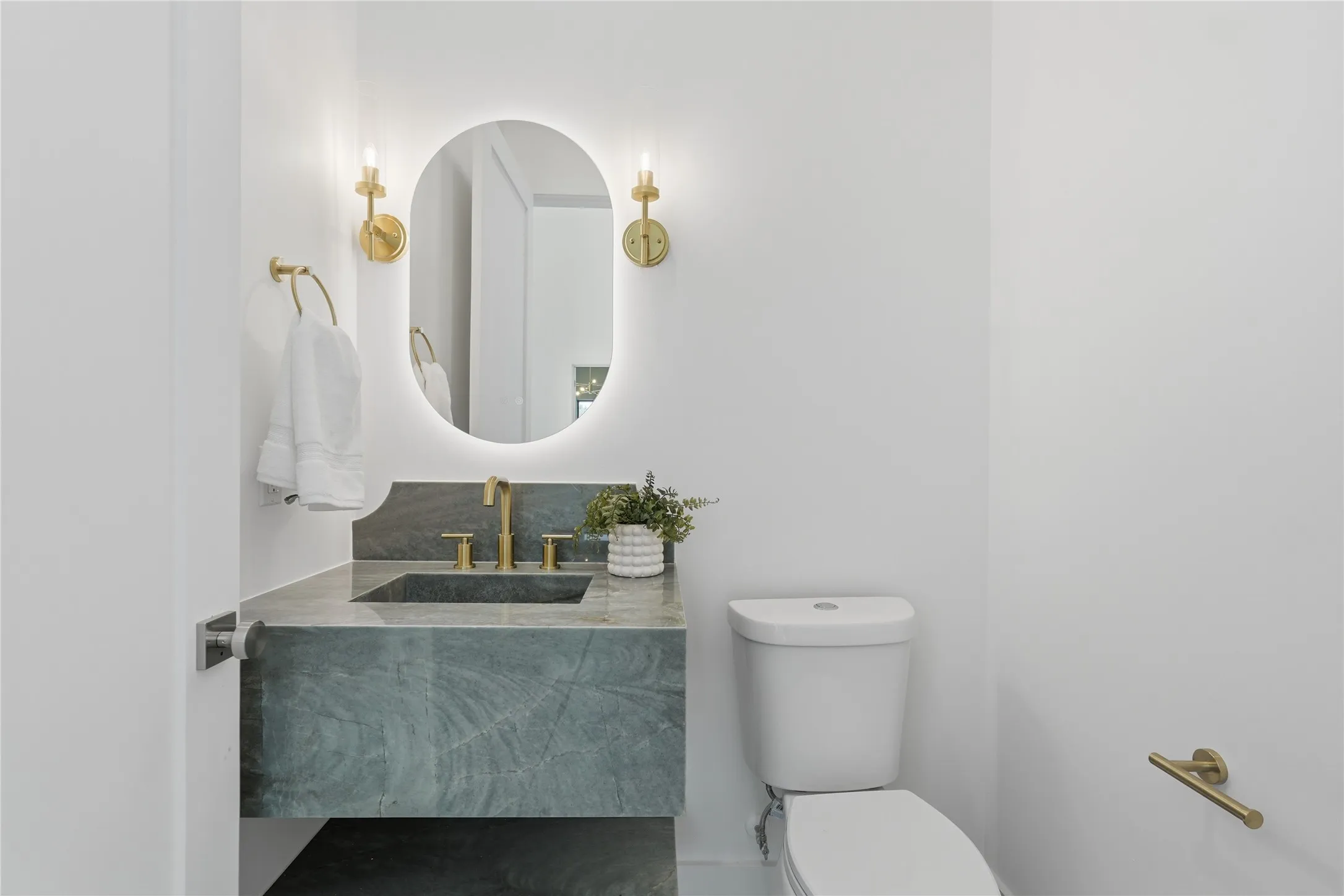 Powder room featuring a floating vanity with an integrated basin, a backlit oval mirror, brass-finish sconces, and a modern toilet