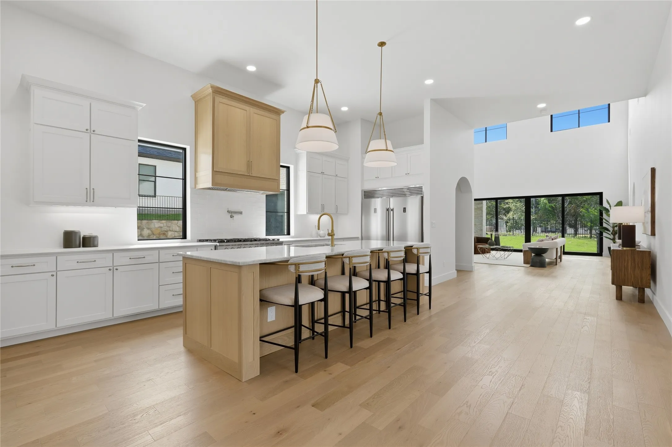 Expansive open-concept kitchen featuring a large central island with seating, integrated appliances, and a wood-finish range hood
