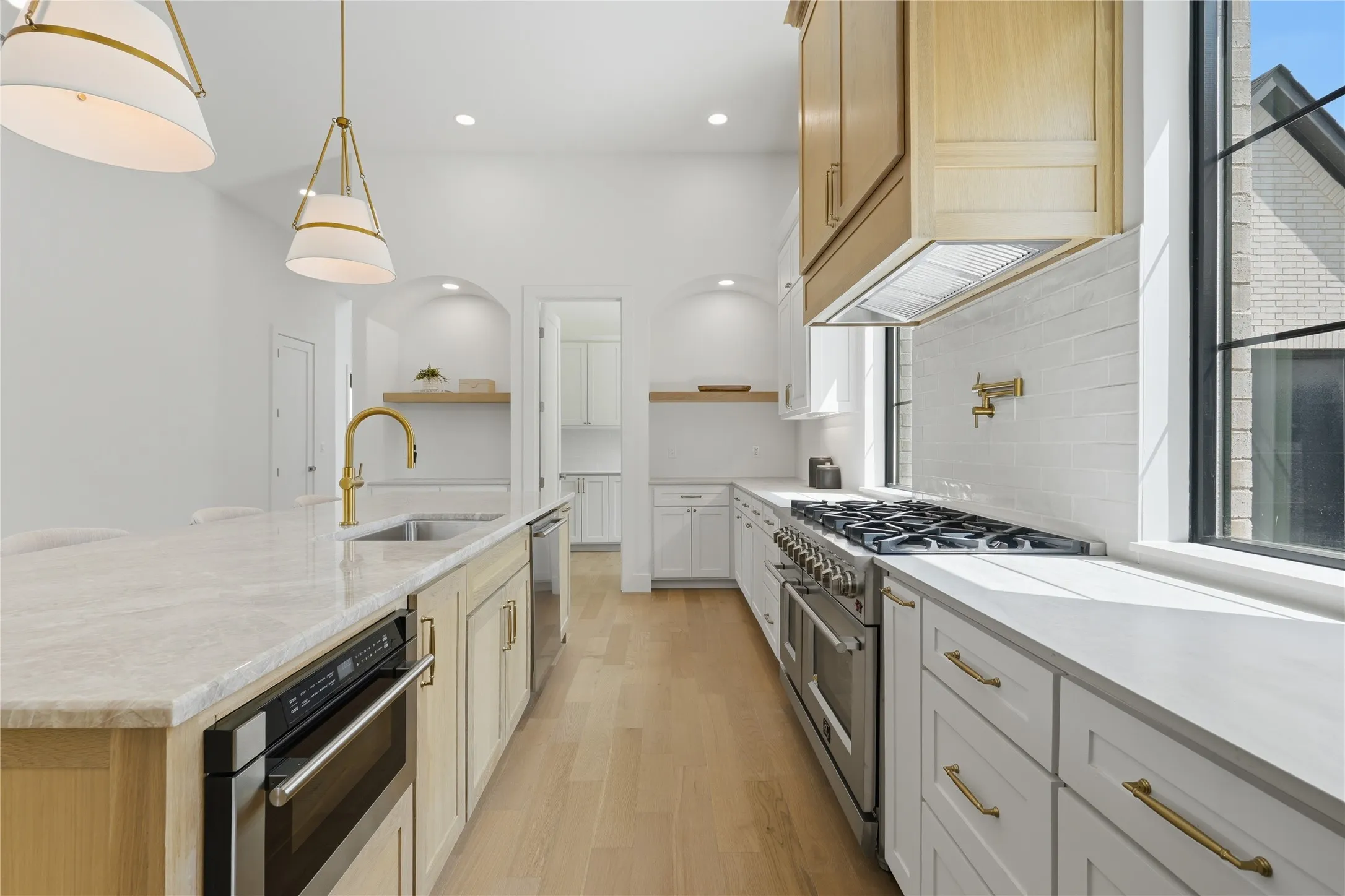 Spacious kitchen featuring a large island with an undermount sink and a built-in microwave, light wood-finish flooring, white perimeter cabinetry, a stainless steel range with a pot filler, and large windows