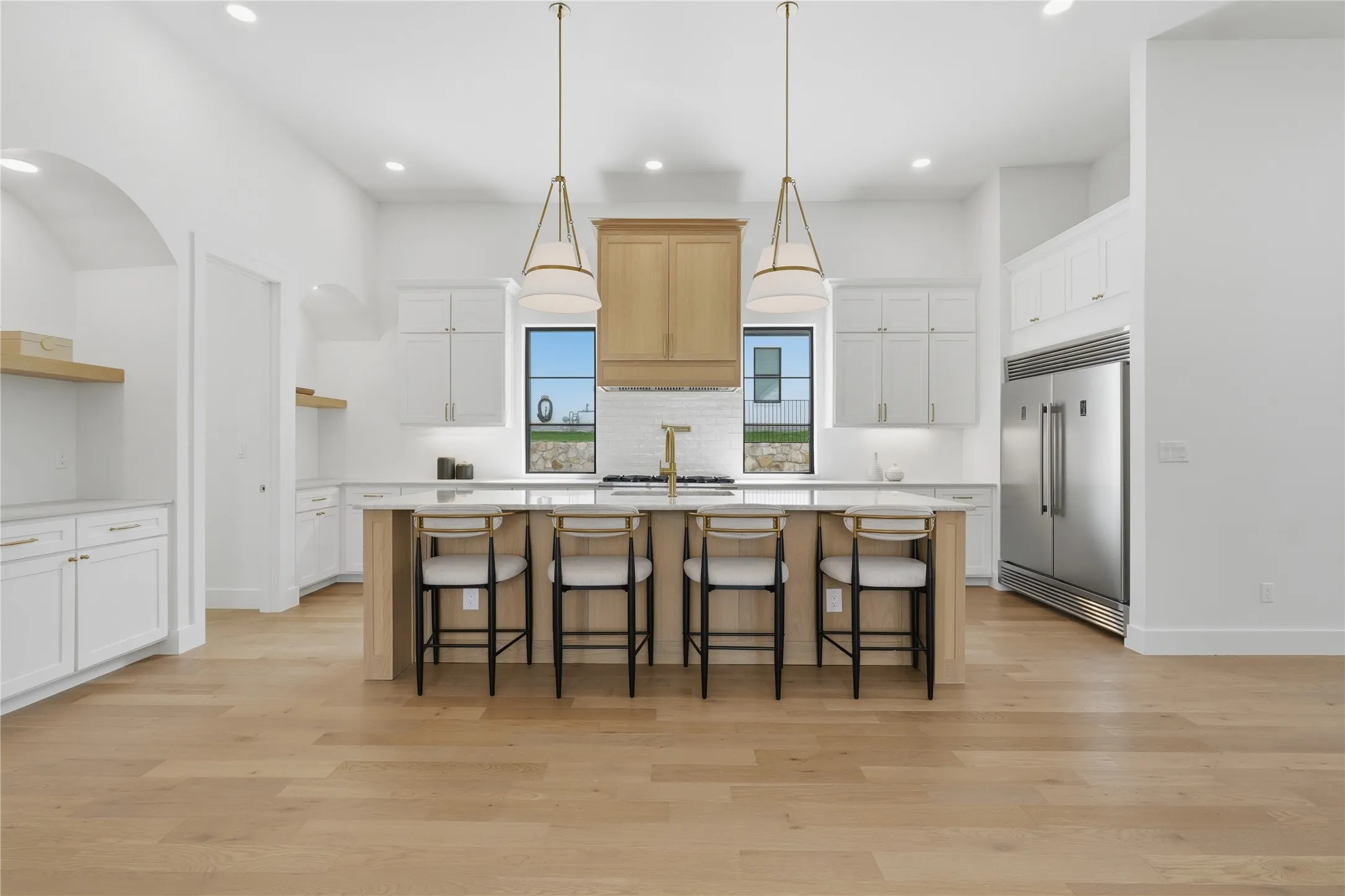 Gourmet kitchen featuring a central island with bar seating, stainless steel appliances, extensive white cabinetry, light wood-finish flooring, and two statement pendant lights
