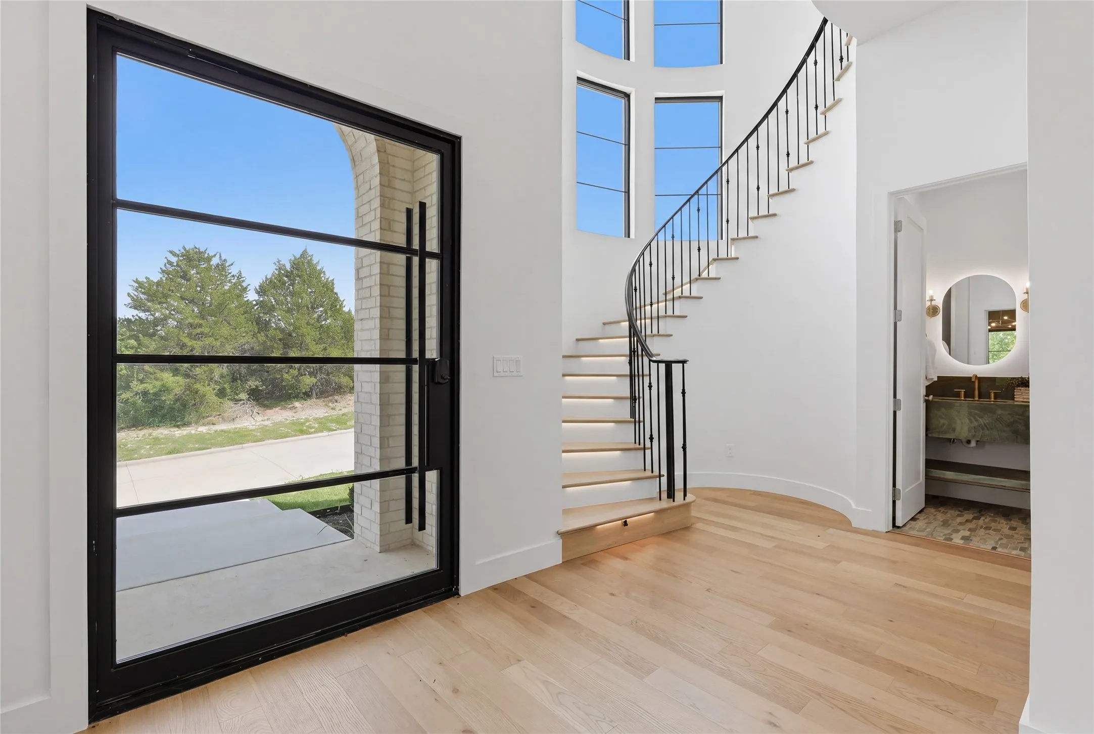 Grand entry featuring a full-light iron and glass door, a sweeping curved staircase with iron balusters, and light wood-finish flooring