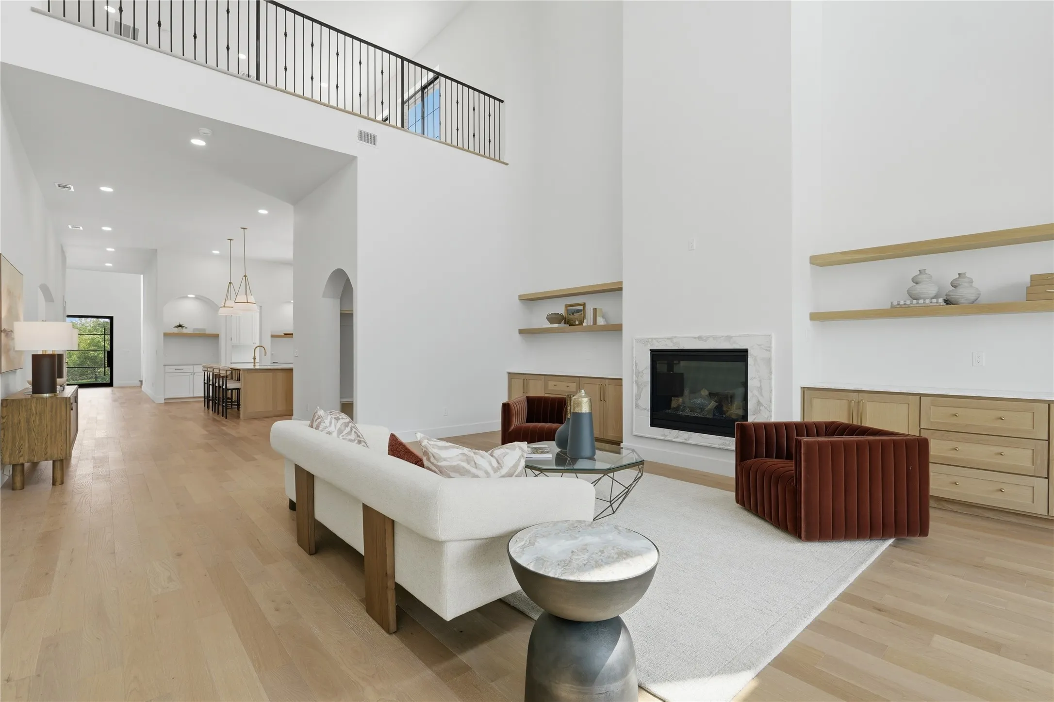 Two-story living area featuring a fireplace with a stone surround, wood-finish flooring, a vaulted ceiling, a loft with a wrought iron railing, and recessed lighting