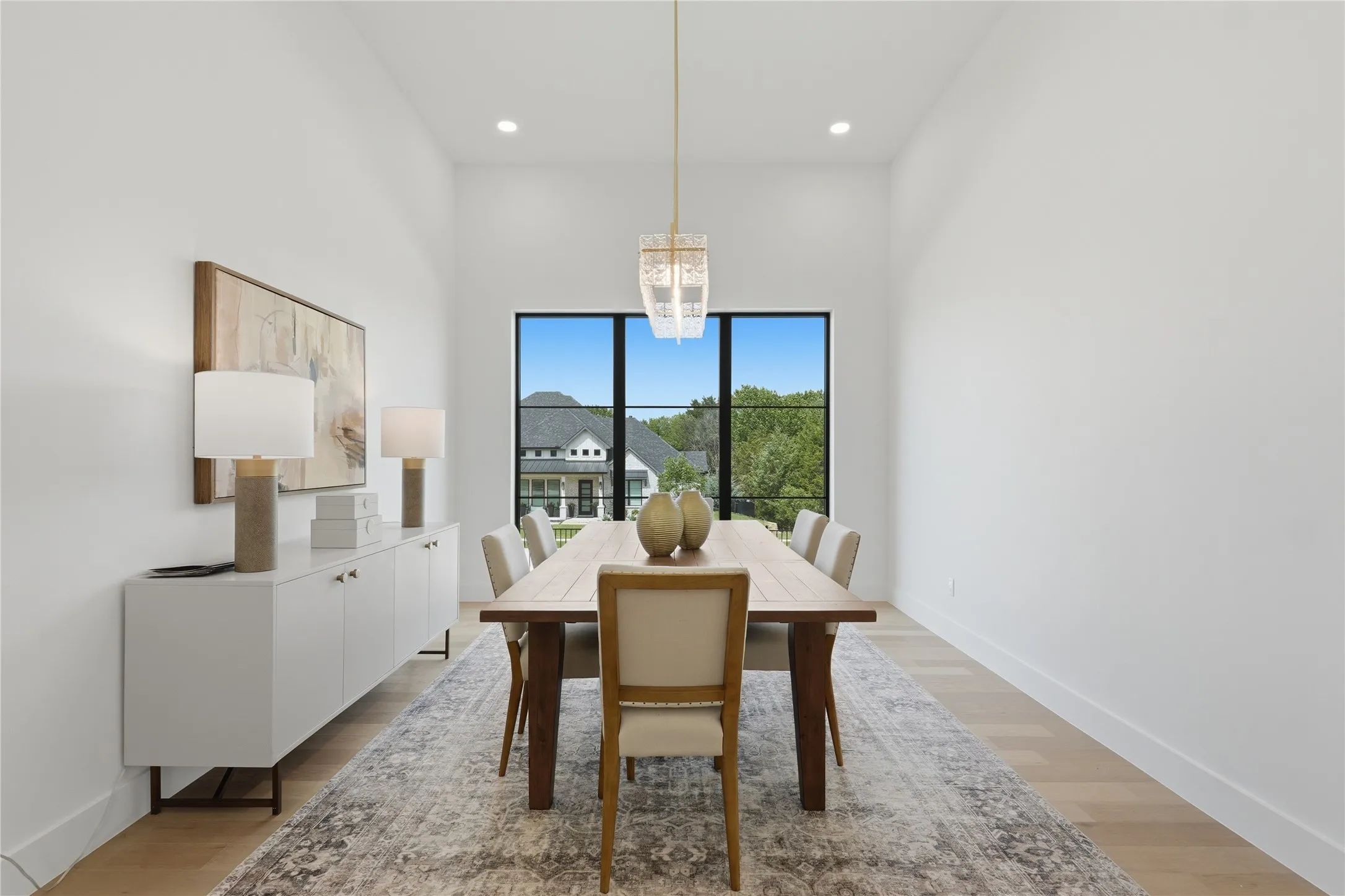 Dining area featuring high ceilings, light wood-finish flooring, a large window with dark trim, and a modern chandelier