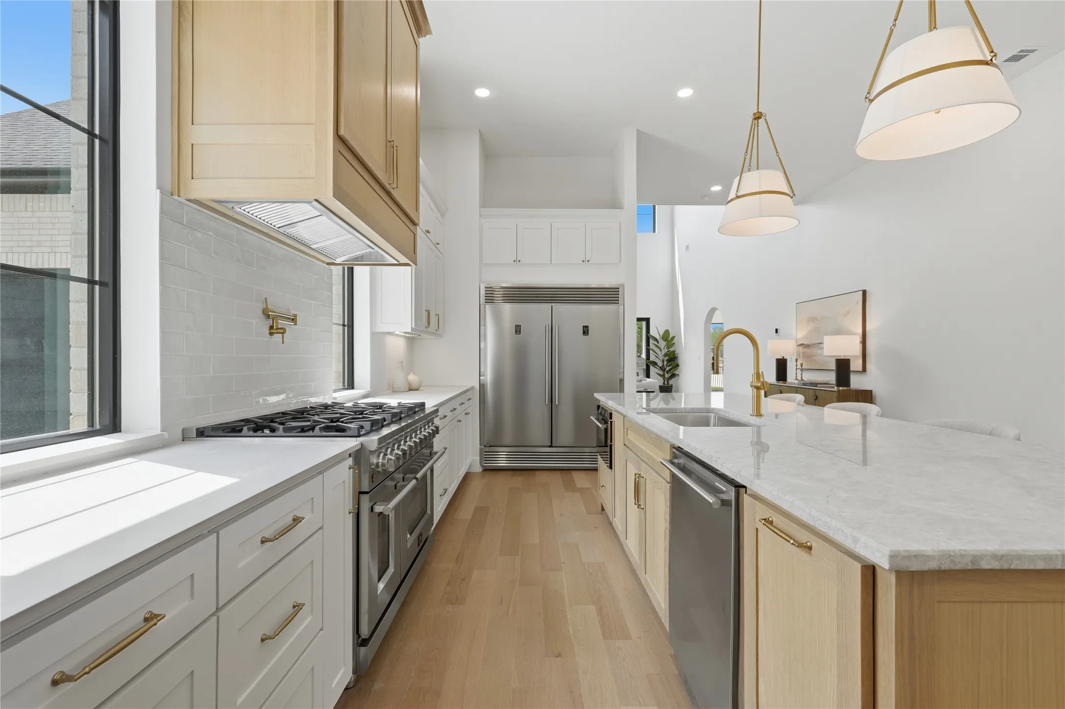 Gourmet kitchen featuring a large island with sink, stainless steel appliances, light wood-finish flooring, white subway tile backsplash, and elegant pendant lighting