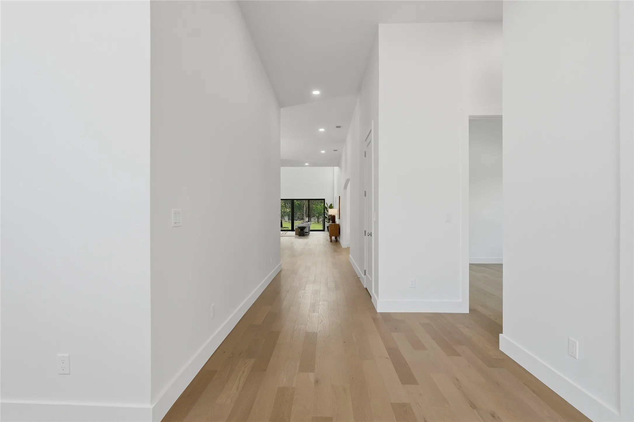 Modern hallway with light wood-finish flooring, recessed lighting, white walls, and high ceilings