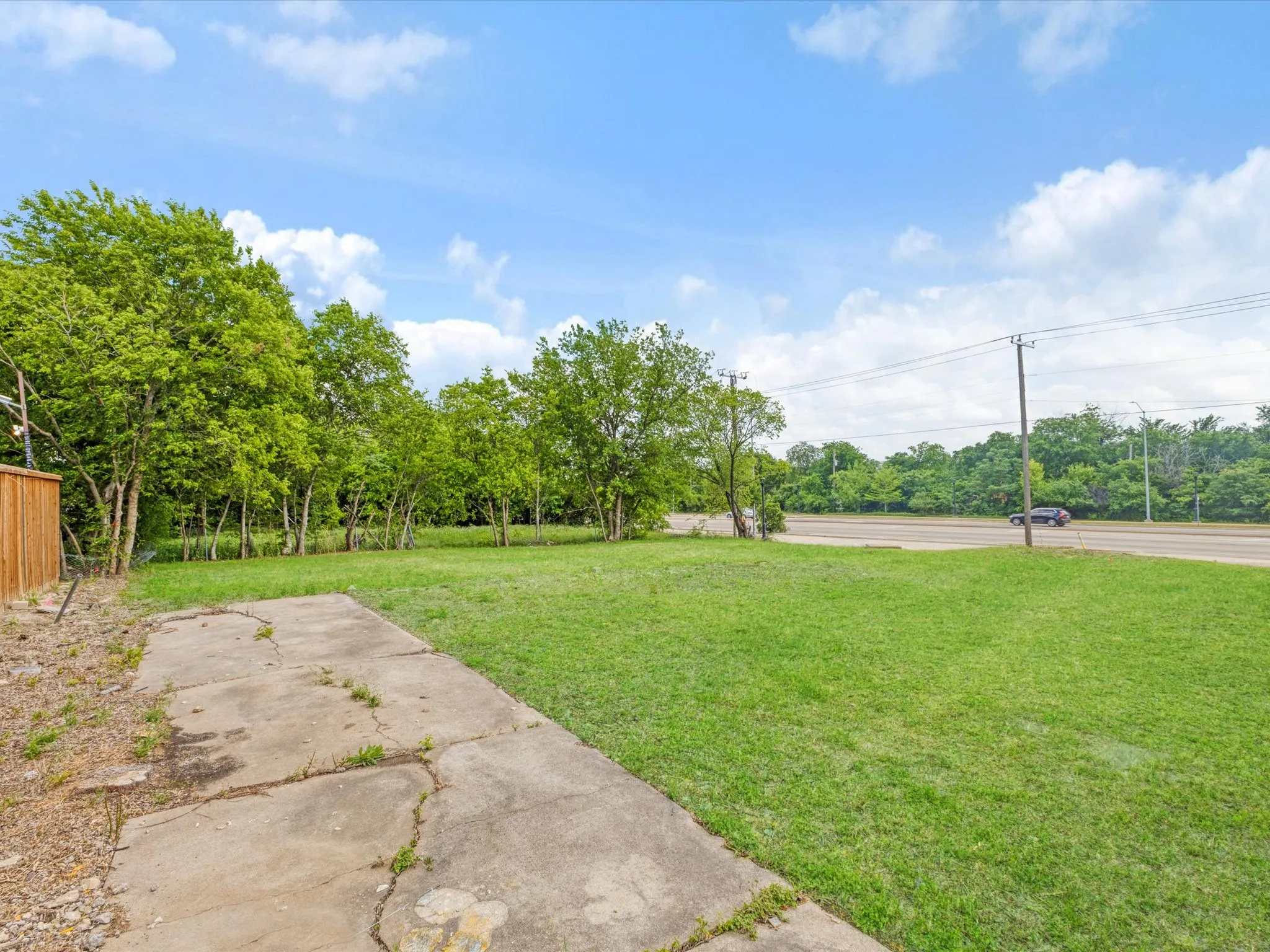 Expansive grass lawn with mature trees and a concrete pad