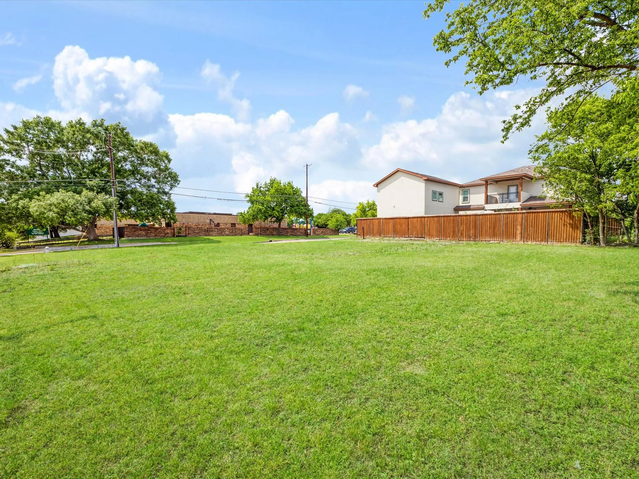 Expansive grassy lot featuring a wooden privacy fence, mature trees, and a two-story structure with a balcony