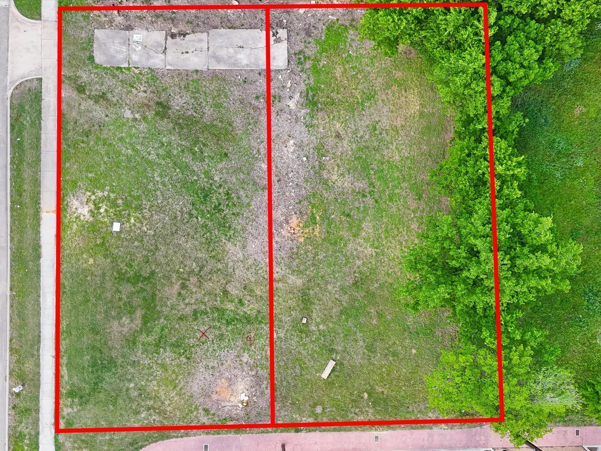 Expansive land parcel featuring existing concrete pads, mature trees, and a paved road frontage