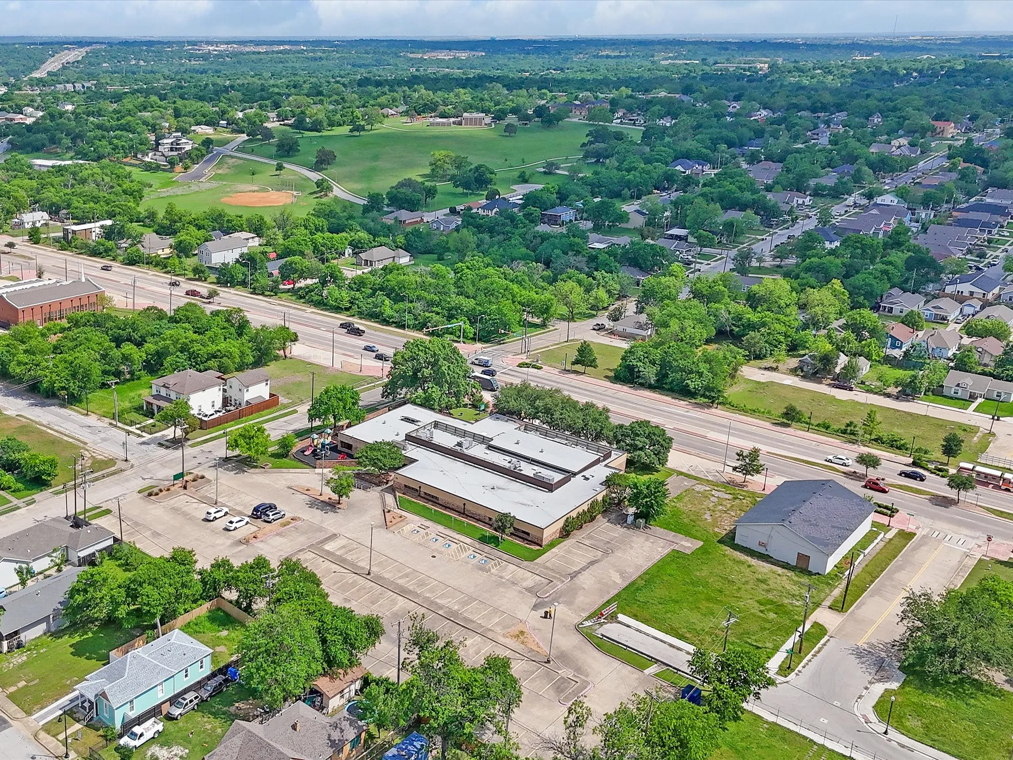 Aerial depiction of commercial building with extensive paved parking, positioned by a multi-lane thoroughfare