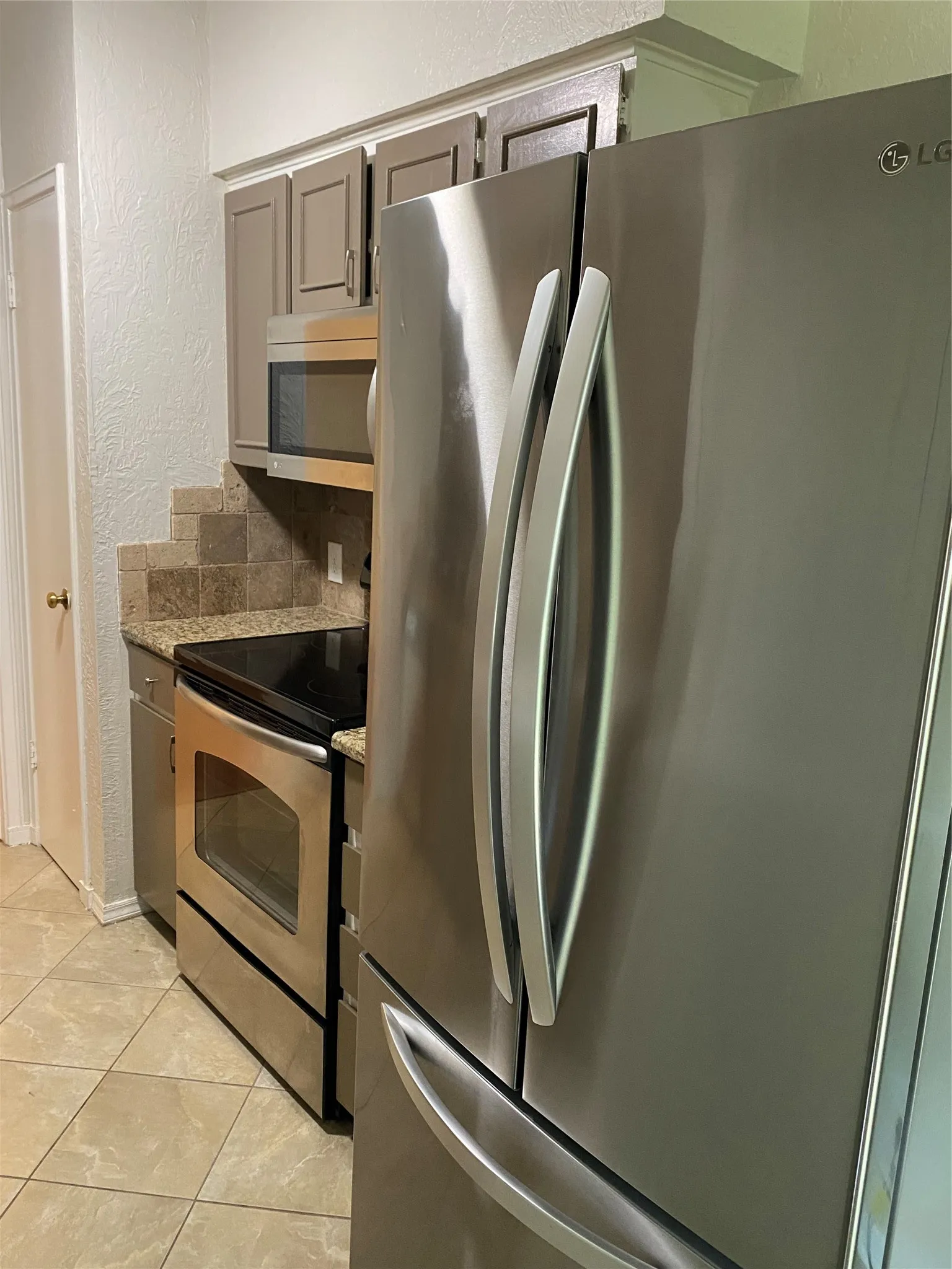 Stainless steel refrigerator, stainless steel oven, stainless steel microwave, stone tile backsplash, tile flooring