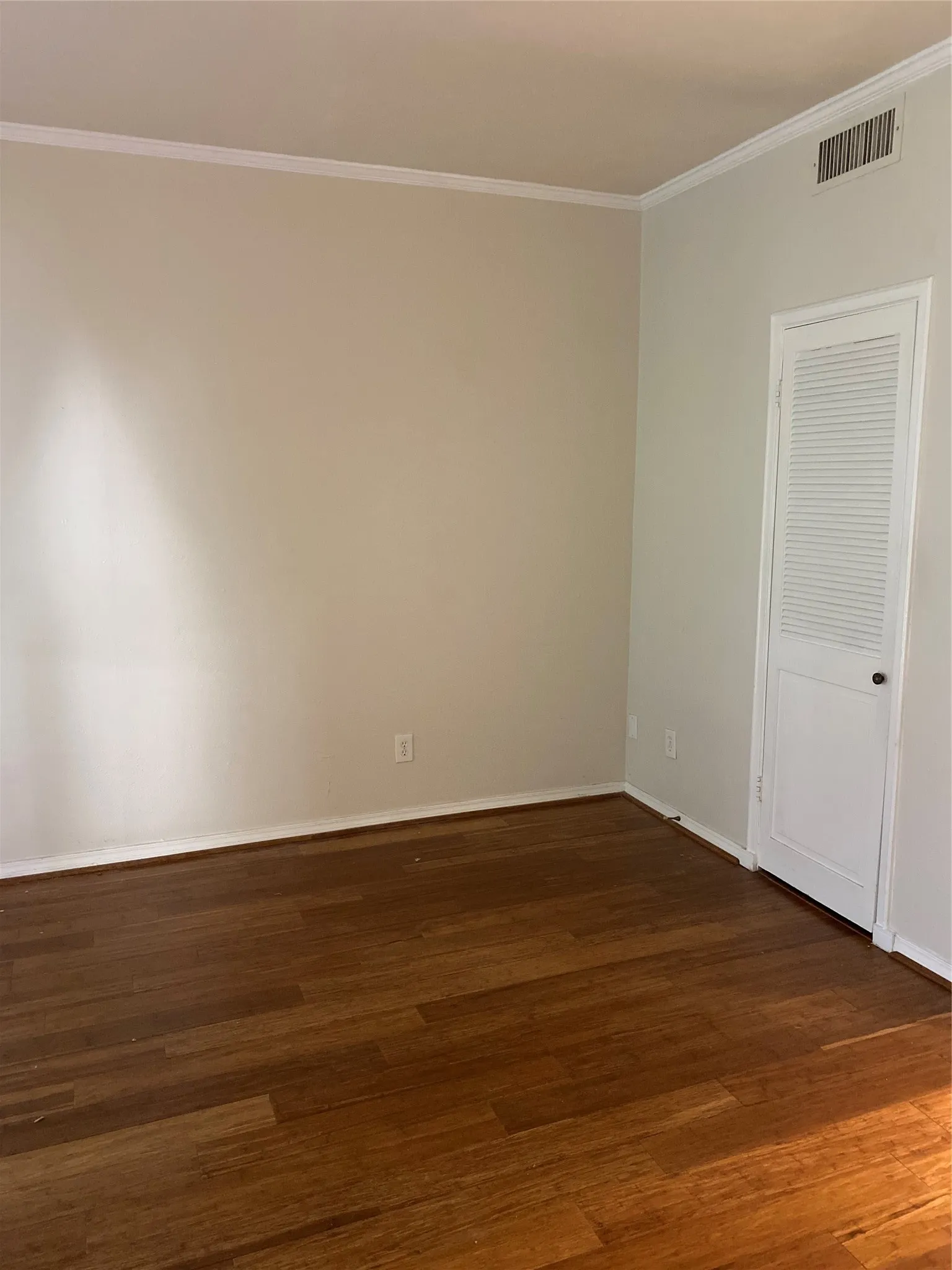 Wood-finish flooring with crown molding and a louvered white door