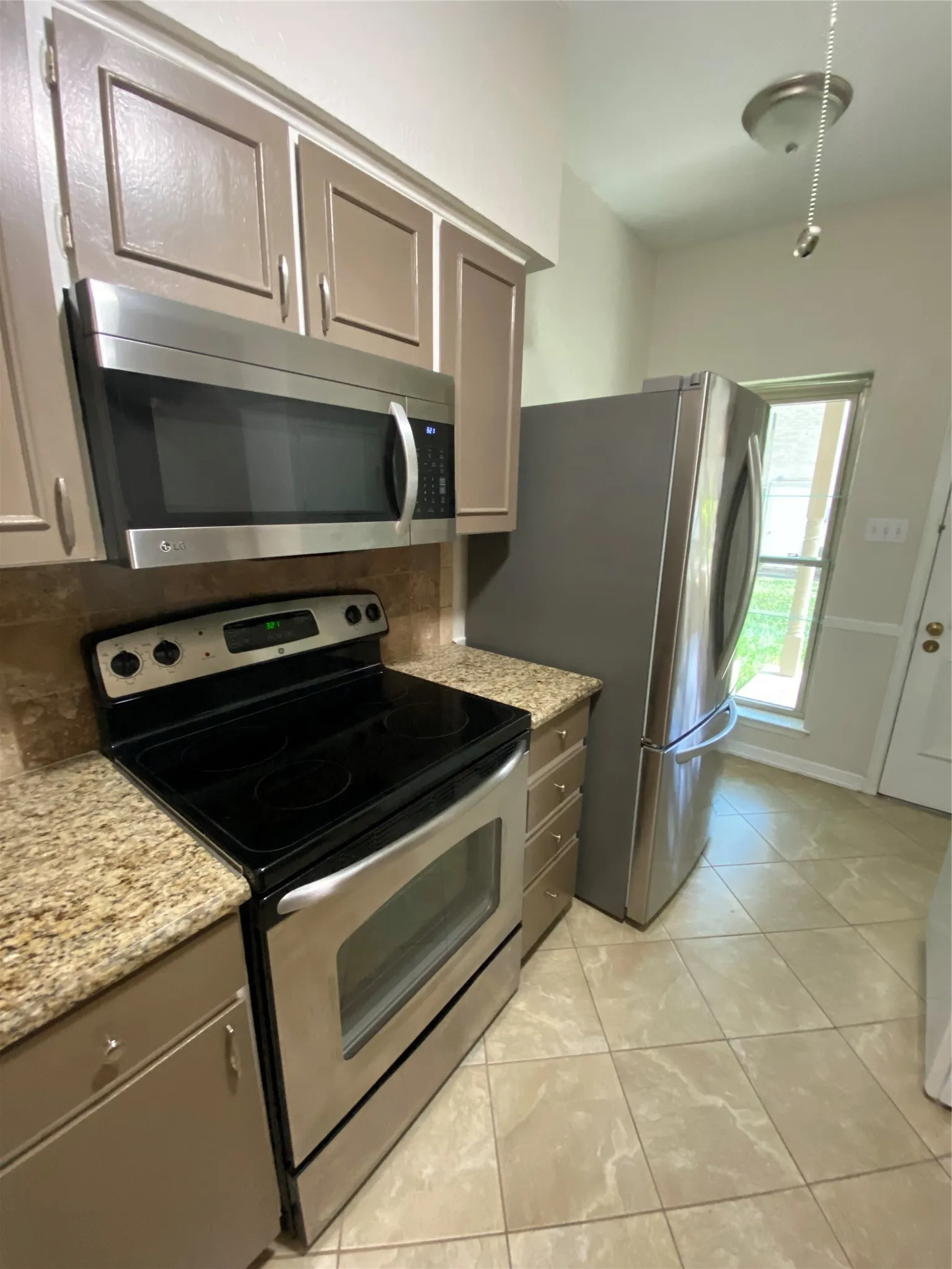 Stainless steel appliances, granite countertops, tile flooring, recessed panel cabinetry, and a ceiling-mounted light fixture