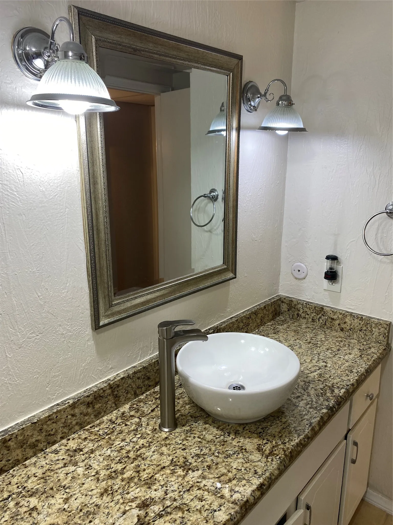 Vanity with granite-style countertop, white vessel sink, brushed nickel faucet, and framed mirror with sconce lighting