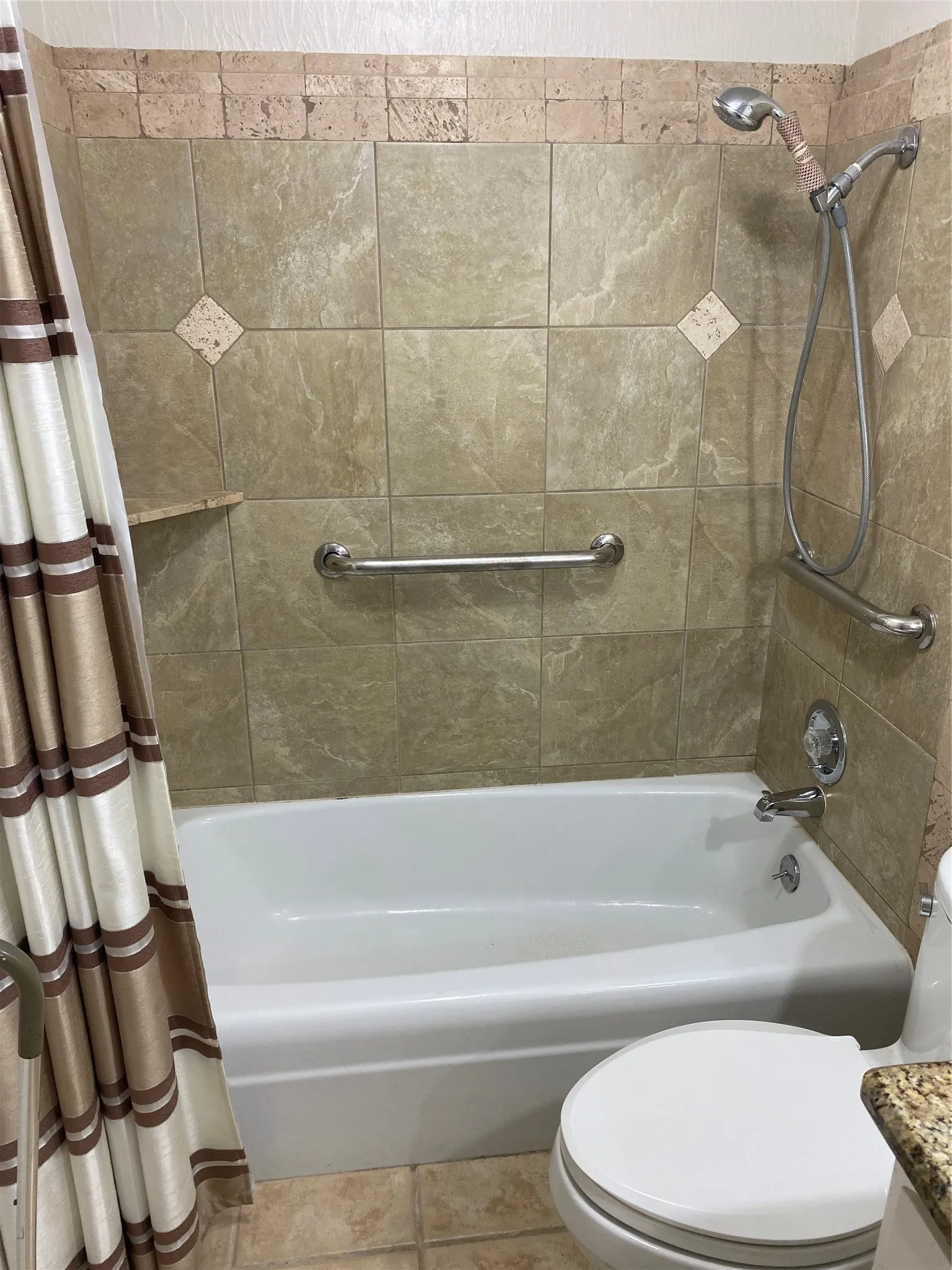 Bathtub with tile surround, built-in grab bars, and a handheld shower fixture