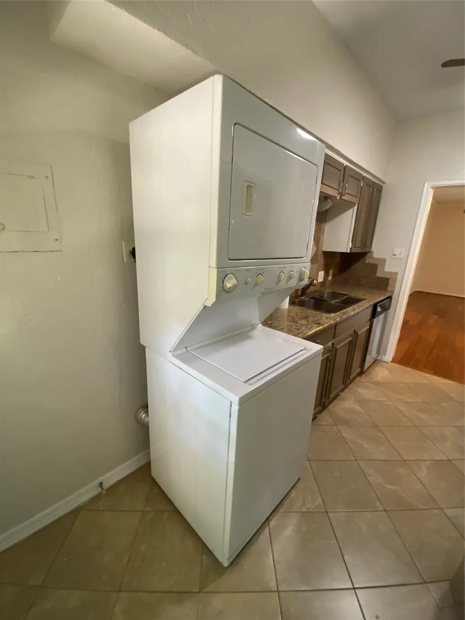 Stacked washer and dryer unit, tile flooring, brown cabinetry, and dark countertops