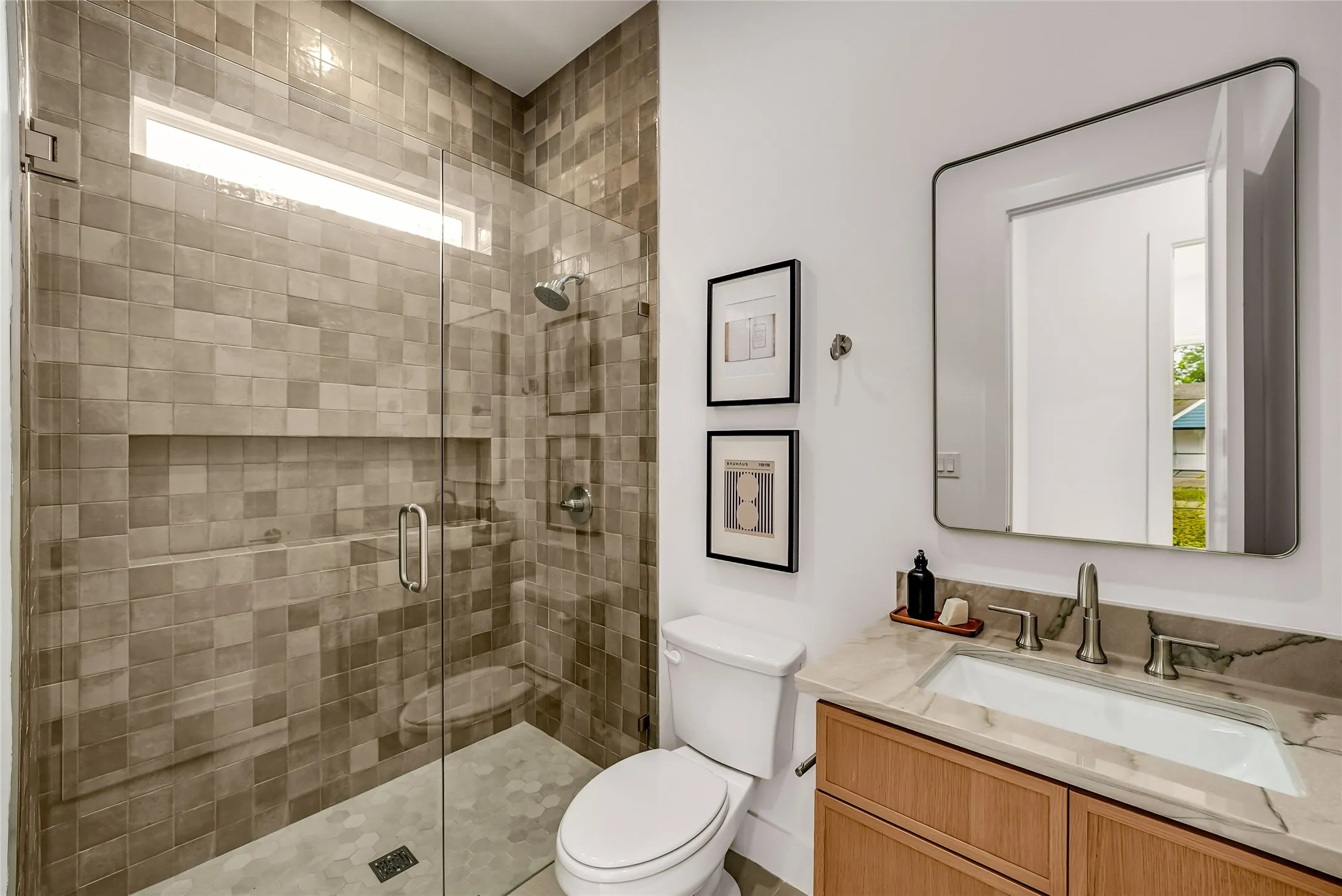 Modern bathroom featuring a glass-enclosed shower with square tile walls and a recessed niche