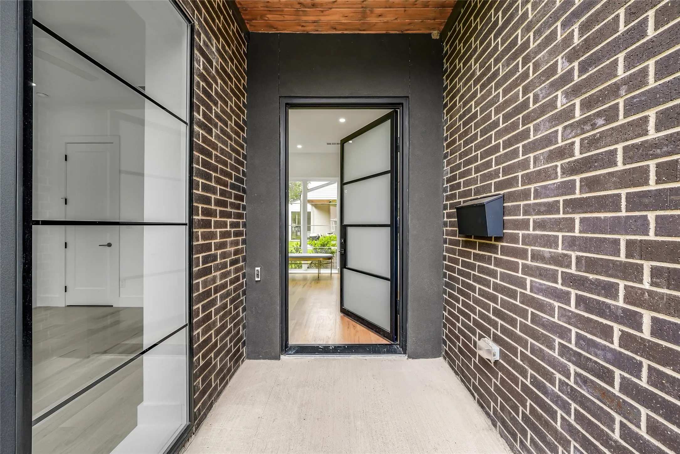 Brick exterior featuring a wooden ceiling accent and a modern black-framed glass entry door