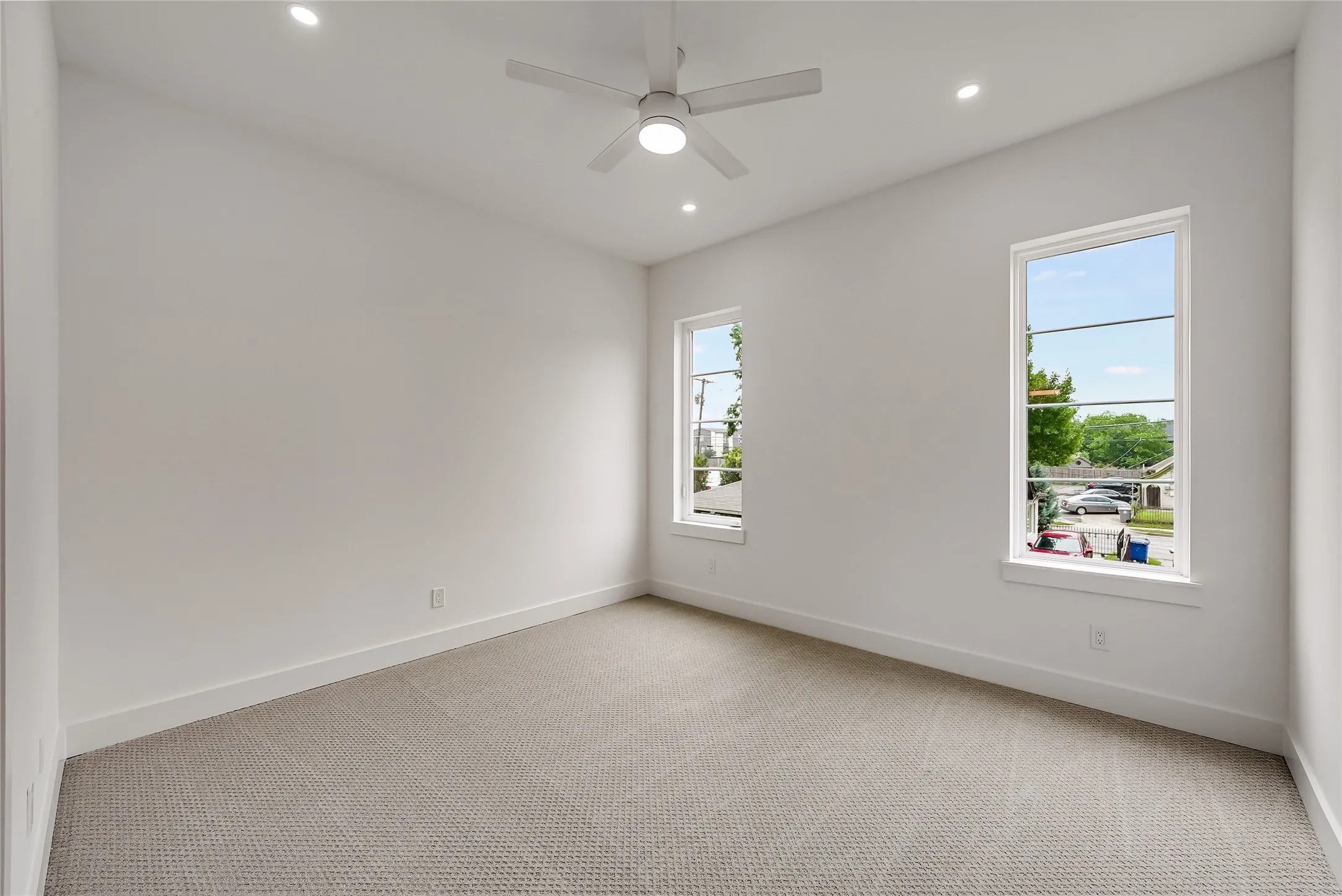 Bright room featuring two large windows, recessed lighting, a ceiling fan, and light-toned carpet flooring