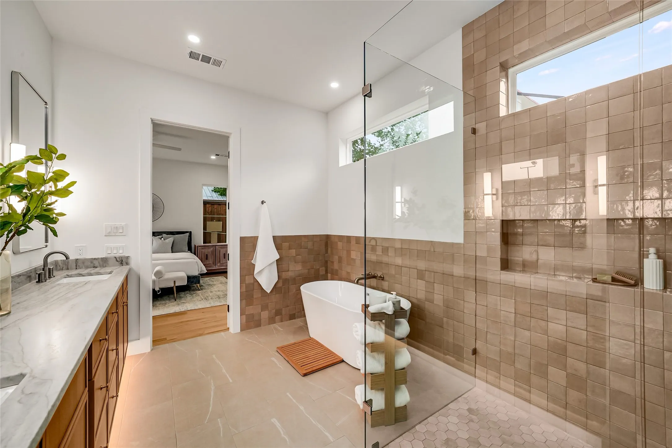Spacious bathroom featuring a freestanding soaking tub, expansive walk-in shower with a glass enclosure, dual vanity with a light-toned countertop, and large format floor tiling