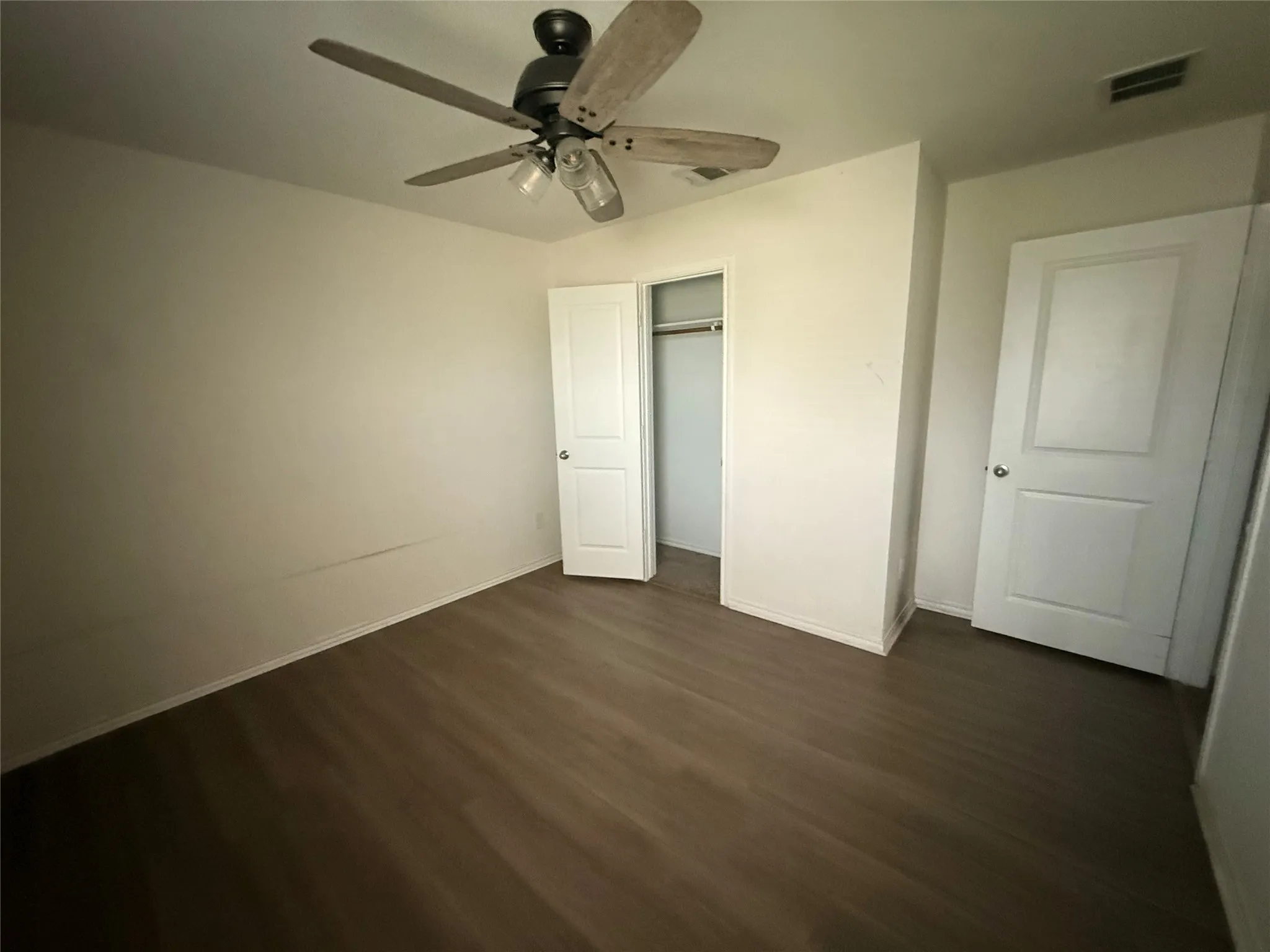Room featuring wood-finish flooring, a ceiling fan with integrated lighting, and a closet with a built-in hanging rod