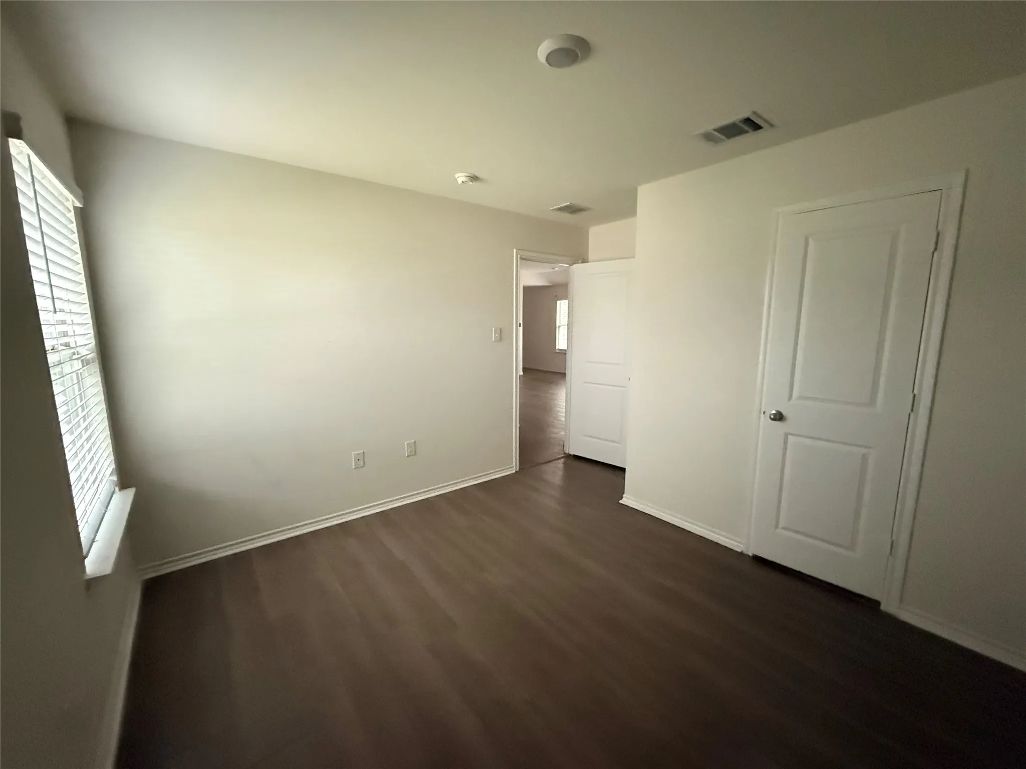 Spacious room featuring wood-finish flooring, white baseboards, and neutral wall paint