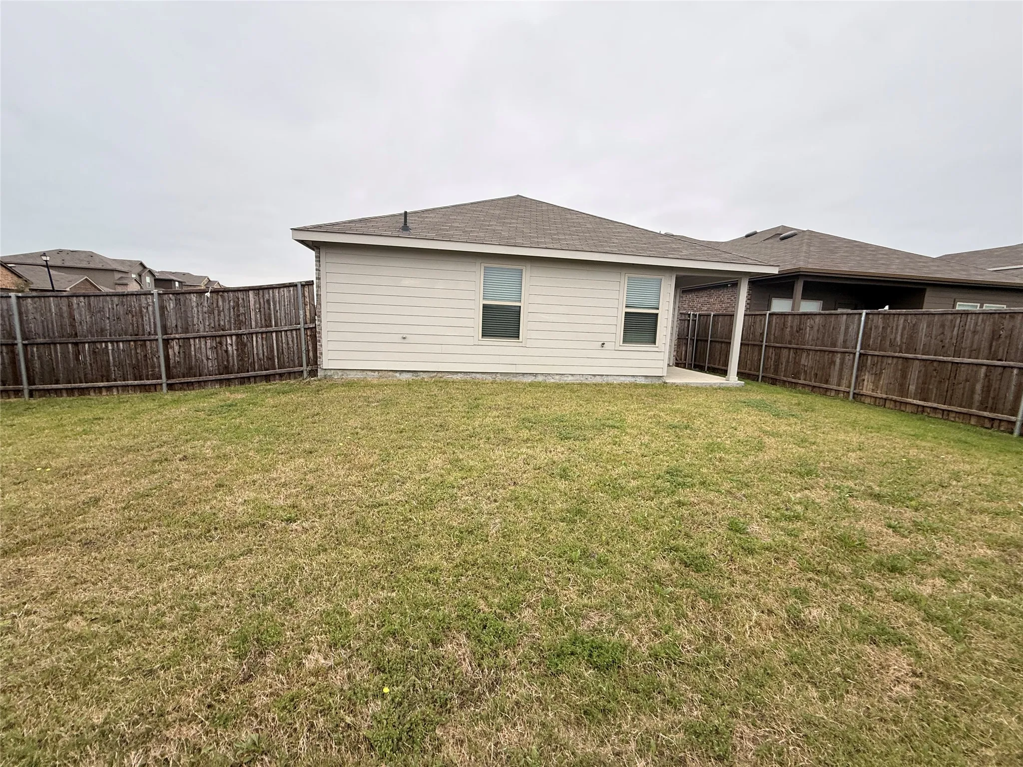 Expansive backyard featuring a wood privacy fence, covered patio with concrete flooring, and a tan siding exterior