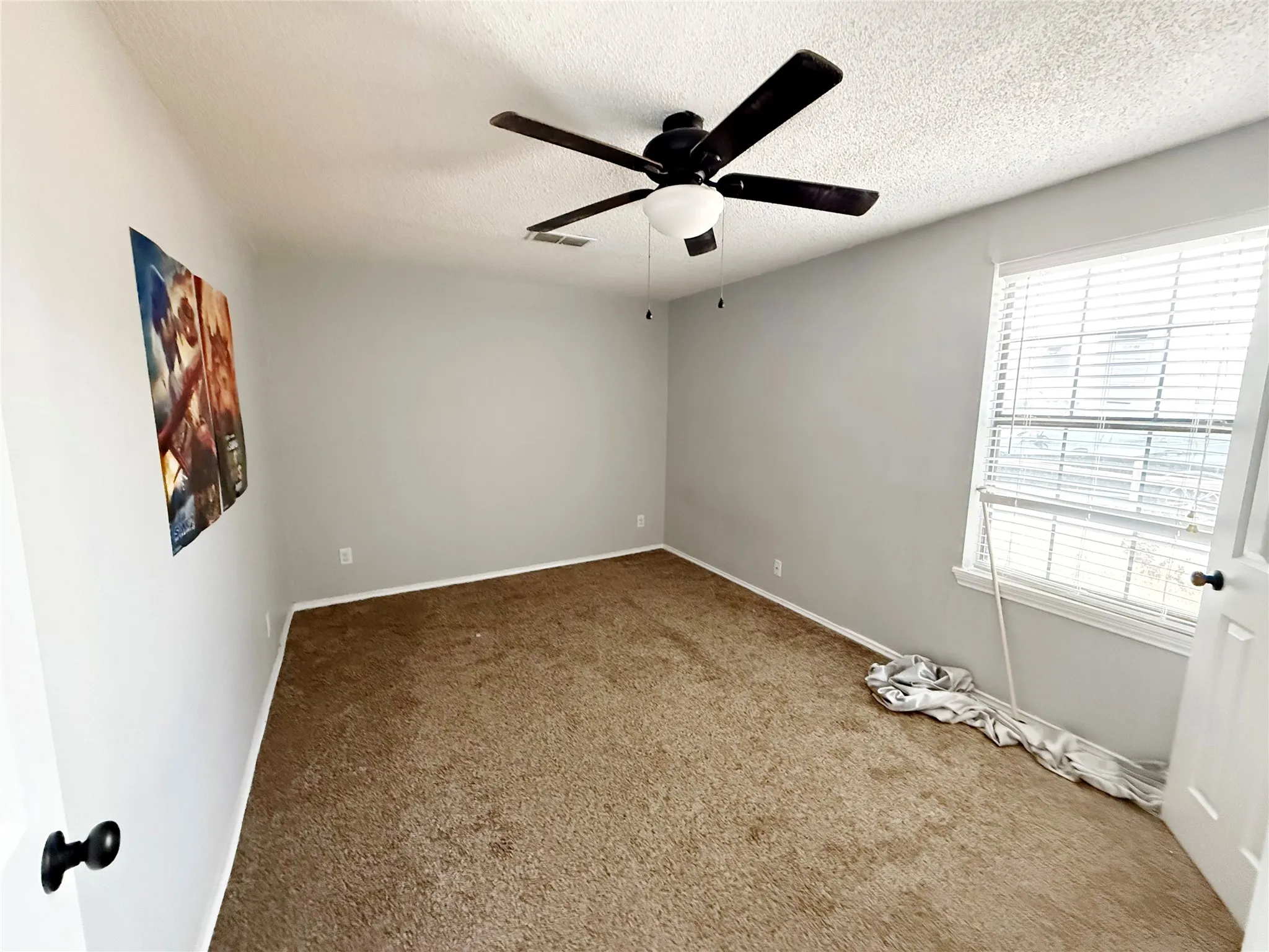 Neutral-toned room featuring light gray walls, textured carpeting, and a ceiling fan with light fixture