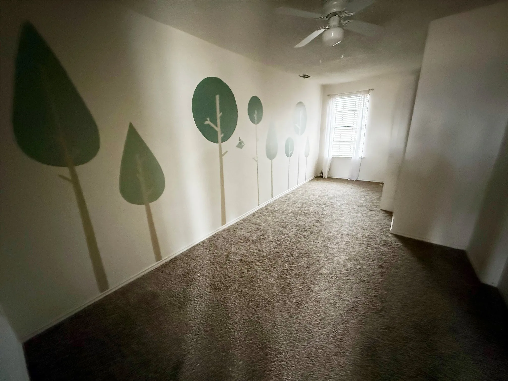 Room featuring wall-mounted tree art, light-colored carpeting, a ceiling fan with light fixture, and window with blinds