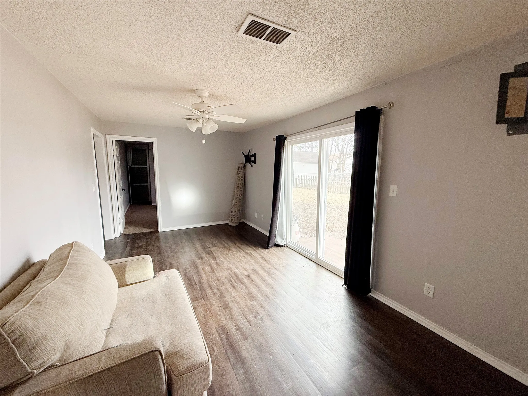 Spacious room featuring wood-finish flooring, light grey wall paint, and a white ceiling fan