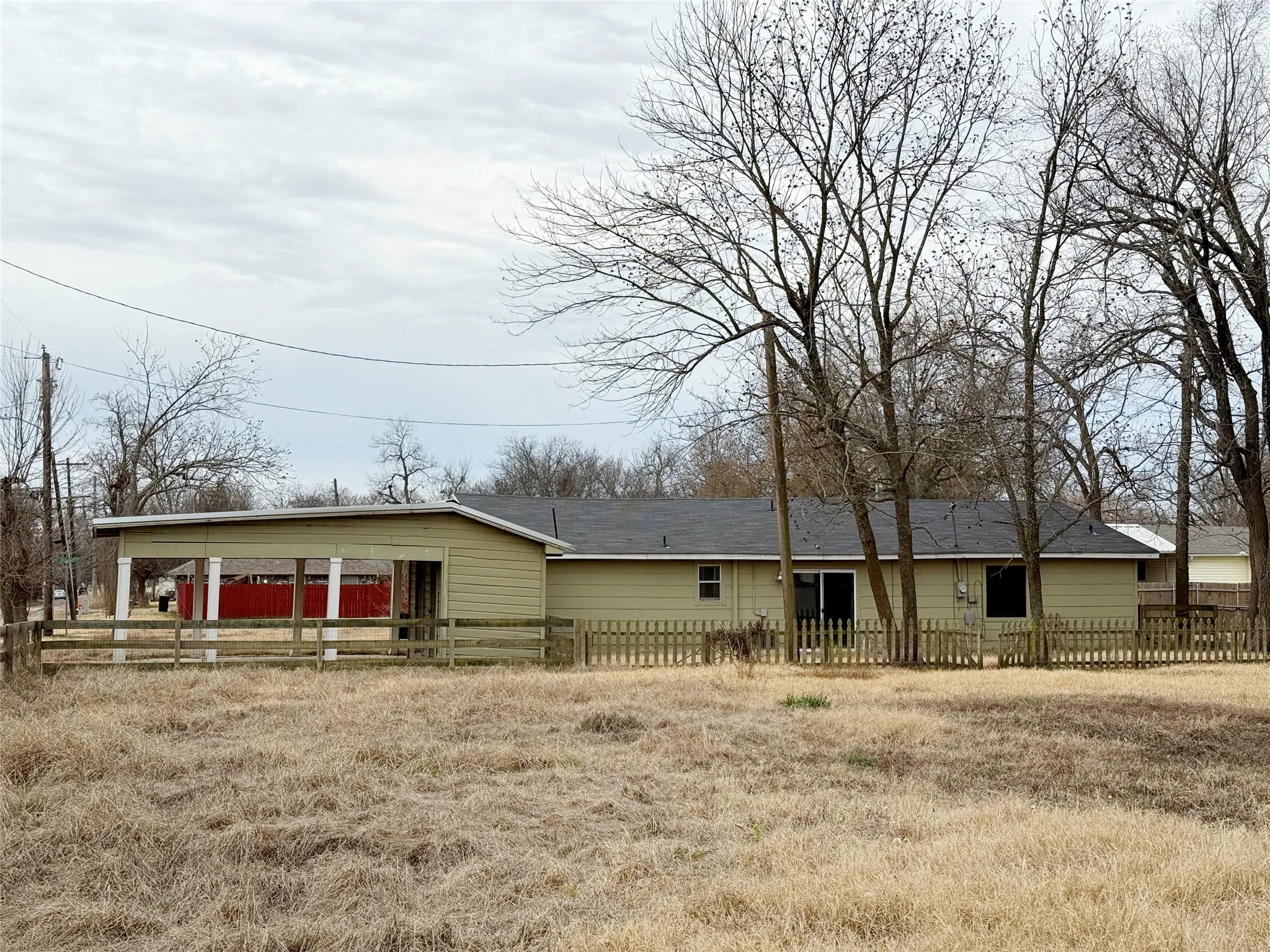 Single-story residence featuring light-colored siding, a dark shingled roof, and a covered carport with white support columns