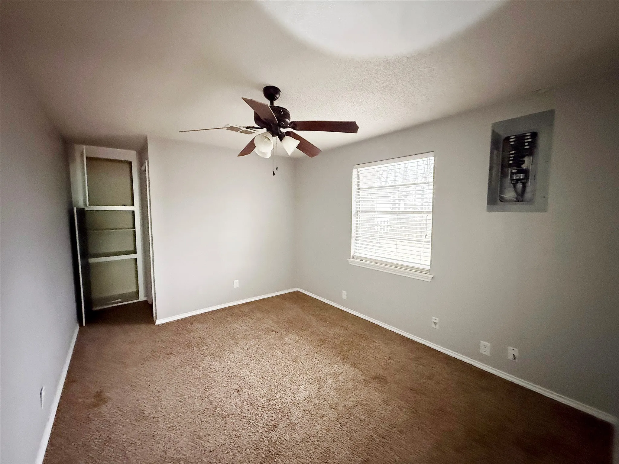 Carpeted interior space featuring light grey walls, a ceiling fan with light fixture, and a window with blinds