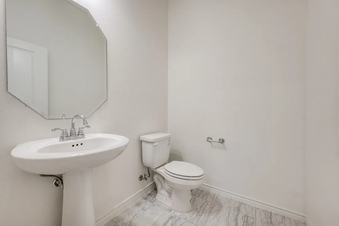 White pedestal sink with chrome faucet, octagonal wall mirror, and a white toilet
