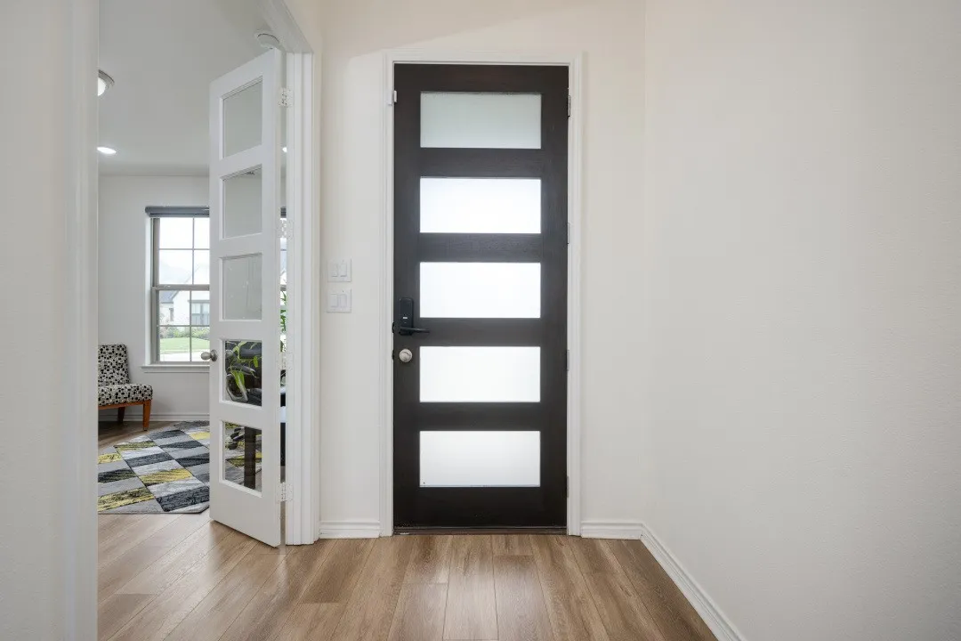 Entryway featuring wood-finish flooring, a contemporary dark-paneled door with frosted glass inserts, and a light-colored interior door with clear glass panels