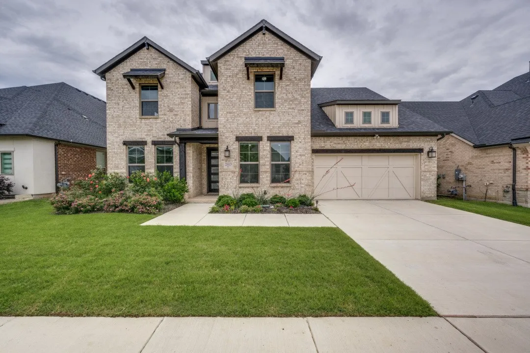 Two-story brick facade residence featuring a dark shingle roof, integrated two-car garage, and dormer window detail