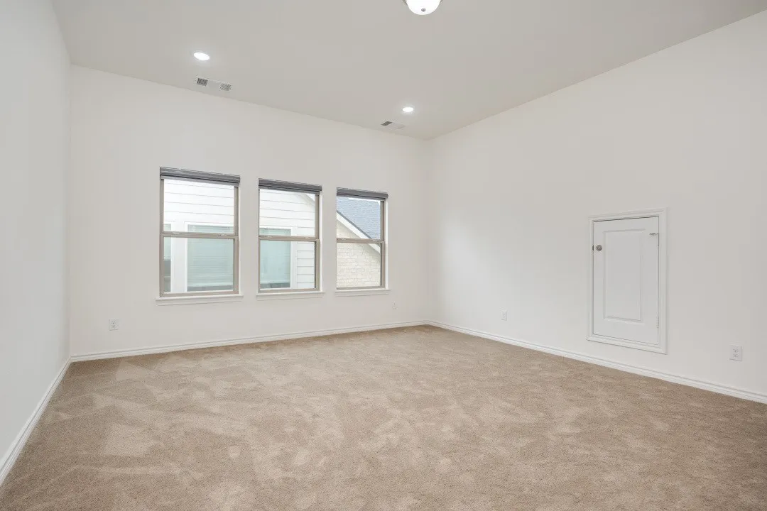 Spacious room featuring three windows, neutral-toned carpet, white walls, and a ceiling with recessed lighting and a flush-mount fixture