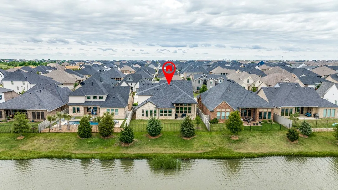 Rear elevation featuring a private swimming pool, fenced backyard, covered patio, and manicured lawn, situated along a body of water