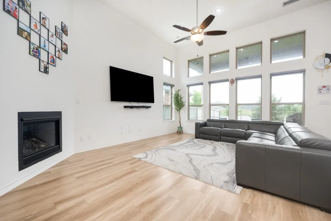 Vaulted ceiling living area featuring a built-in fireplace, wood-finish flooring, a ceiling fan with integrated lighting, and multiple large windows