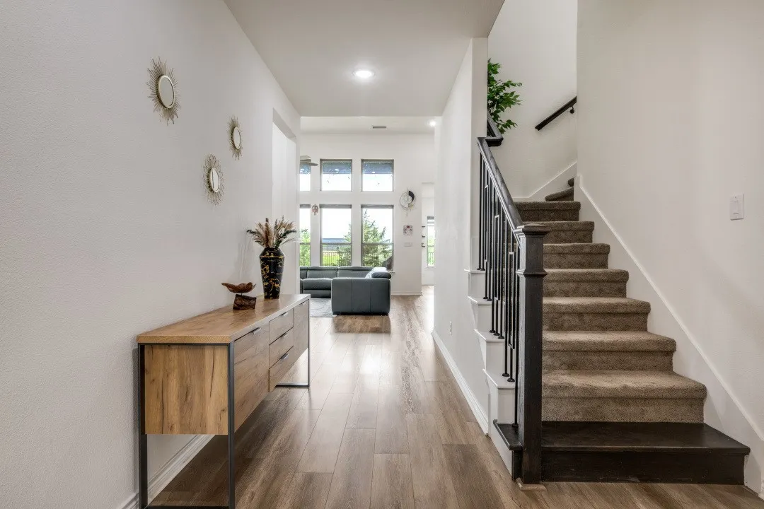 Foyer featuring wood-finish flooring extending into the main living space, a carpeted staircase with dark wood newel posts and handrail, and an open concept beyond