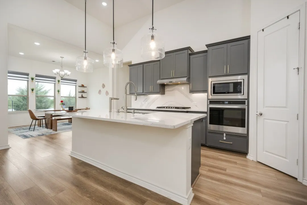 Modern kitchen featuring a large central island with a waterfall countertop, gray cabinetry, built-in stainless steel appliances, and wood-finish flooring