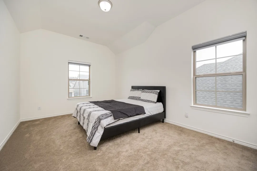 Carpeted room featuring a vaulted ceiling, two windows with blinds, and a flush-mount ceiling light fixture