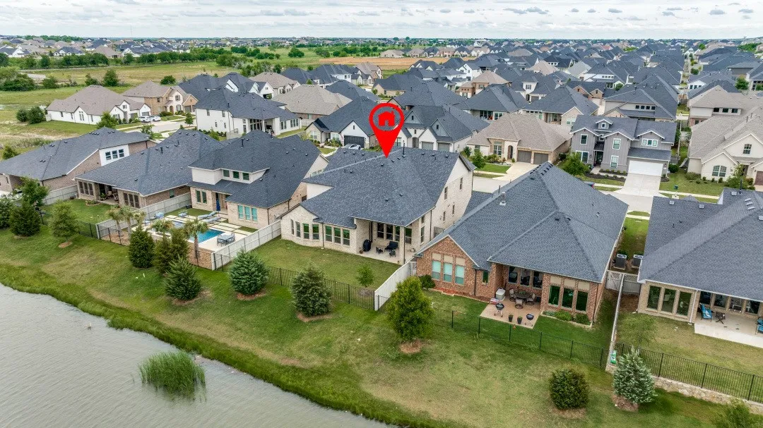 Aerial perspective of a residential community featuring a prominent lakefront property with a dark shingle roof